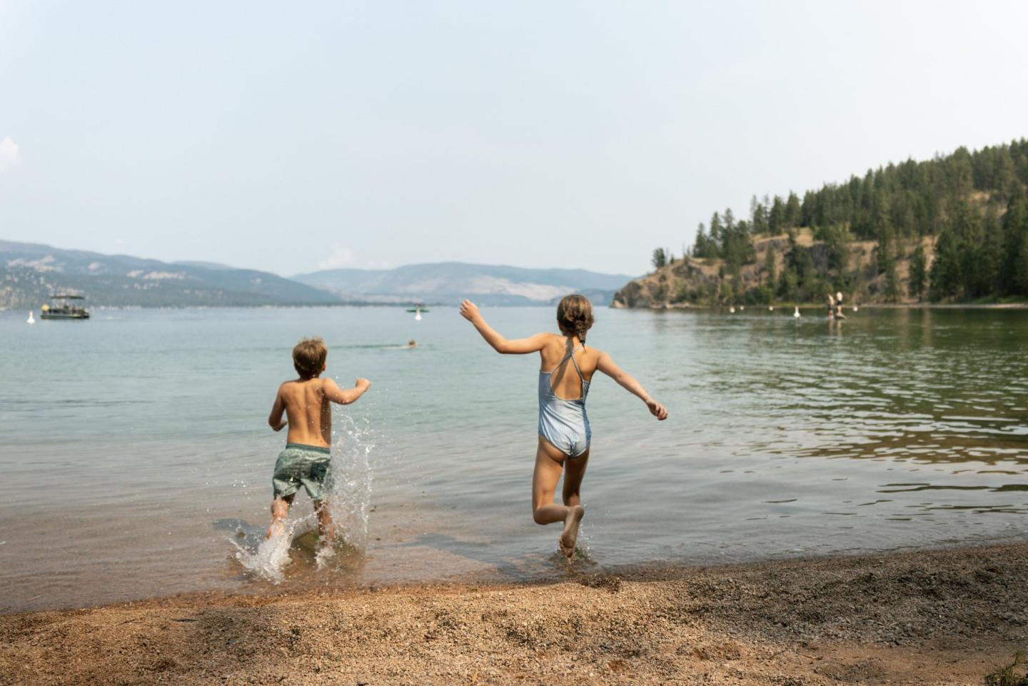 Two children run into a calm lake on a sunny day.