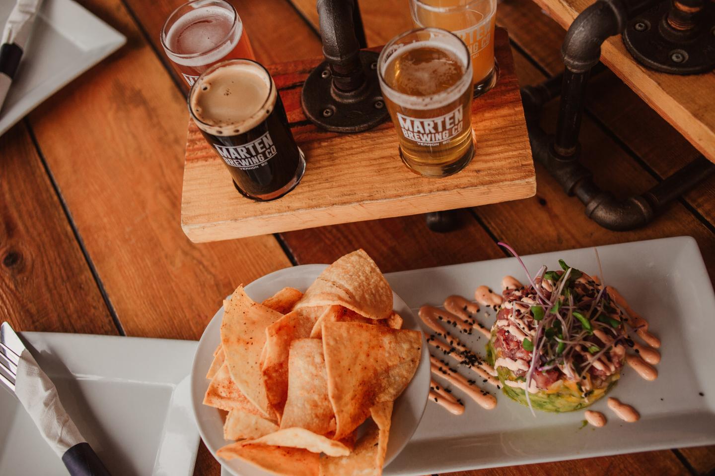 a flight of beers and a bowl of tortilla chips with guacamole