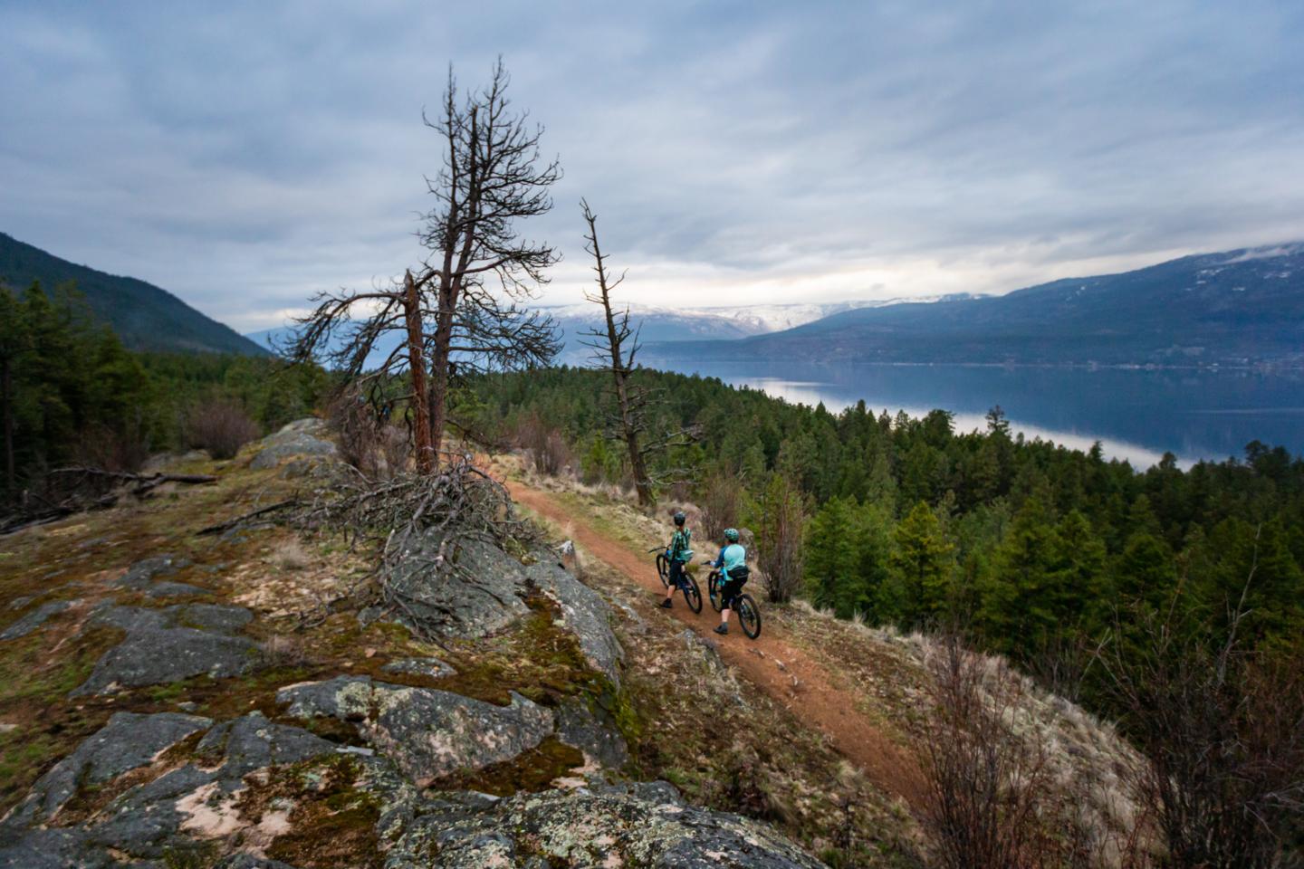 Two mountain bikers on a mountain overlooking a lake
