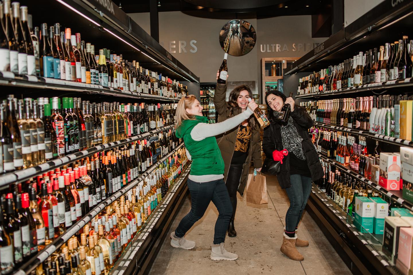 women laughing in wine aisle of store