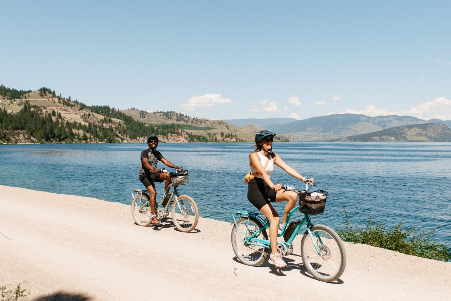 two people riding bikes alongside lake