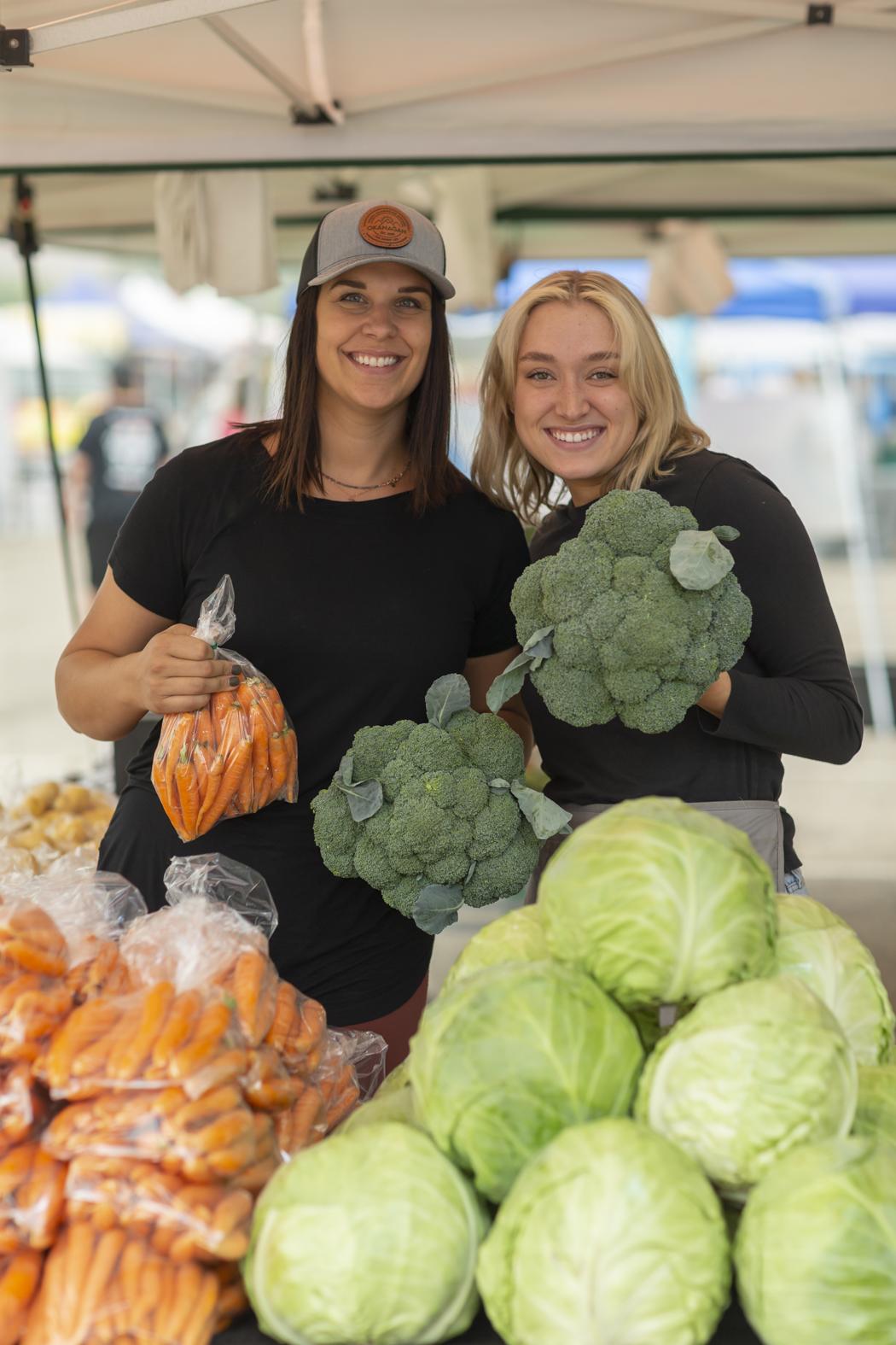 Women holding up fresh veggies at Vernon Farmers Market