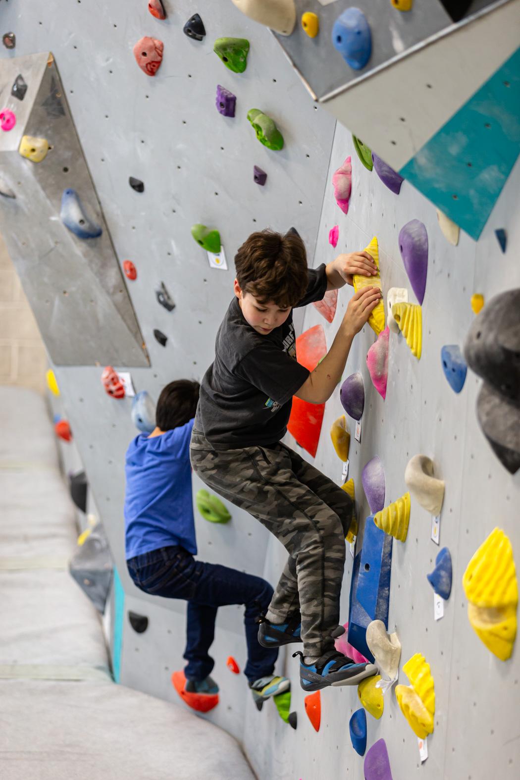 Two children rock climing on an indoor rock climbing wall