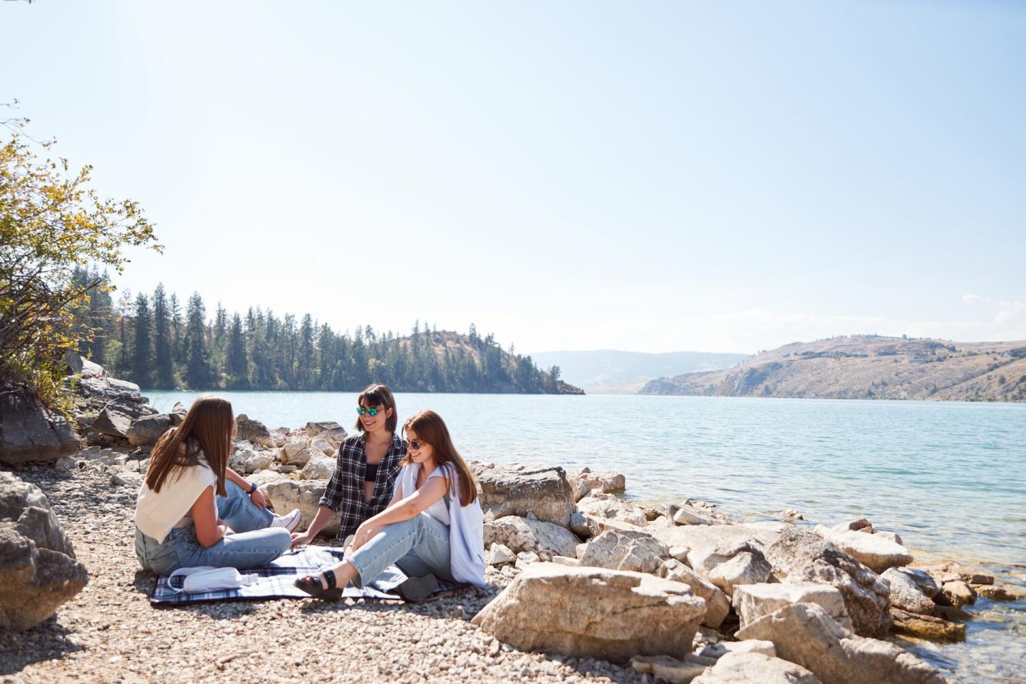A small group of women sitting on the shore of Juniper Bay in Vernon BC