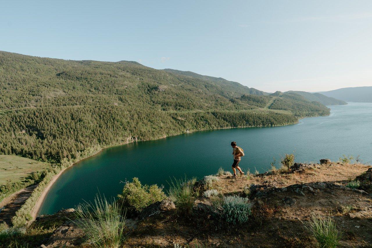 Man walking along a mountain trail looking down on a sandy beach and turquoise waters