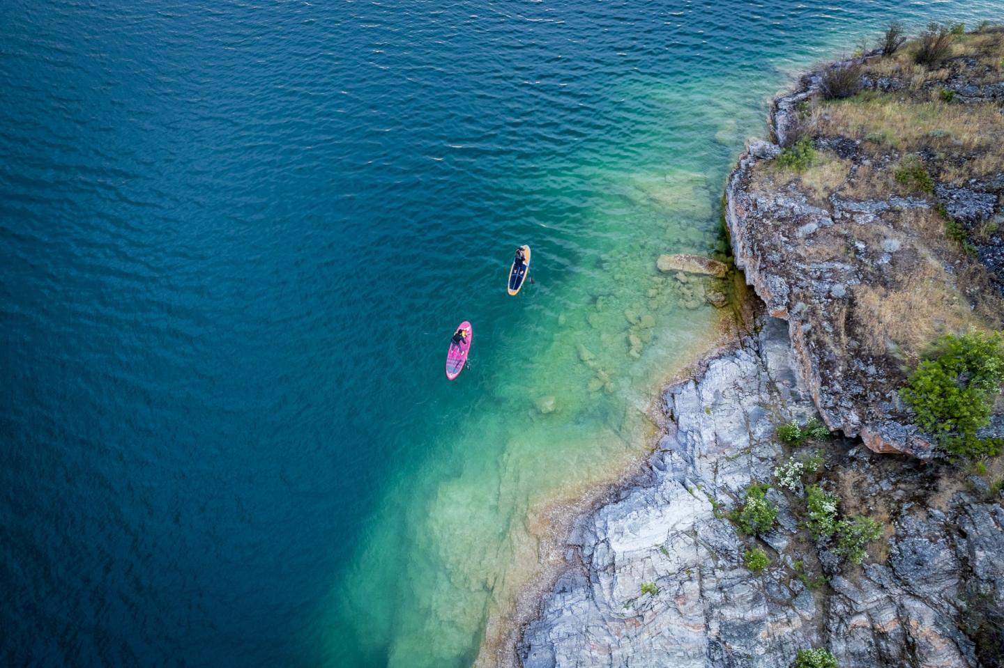 two paddleboarders along a rocky shoreline