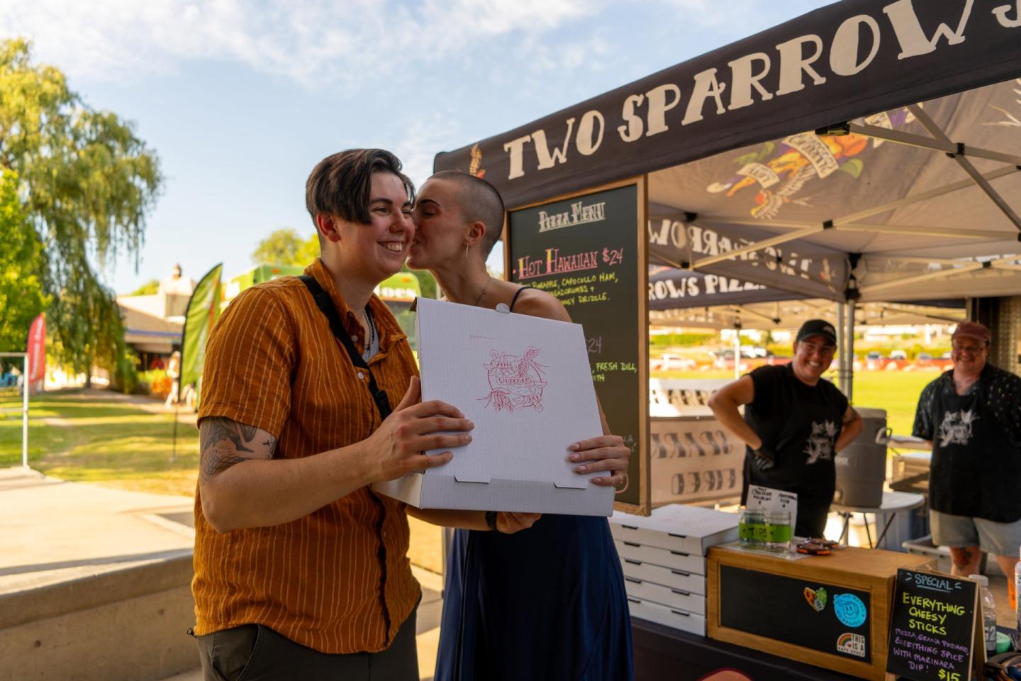 couple with pizza box outside of food truck at market
