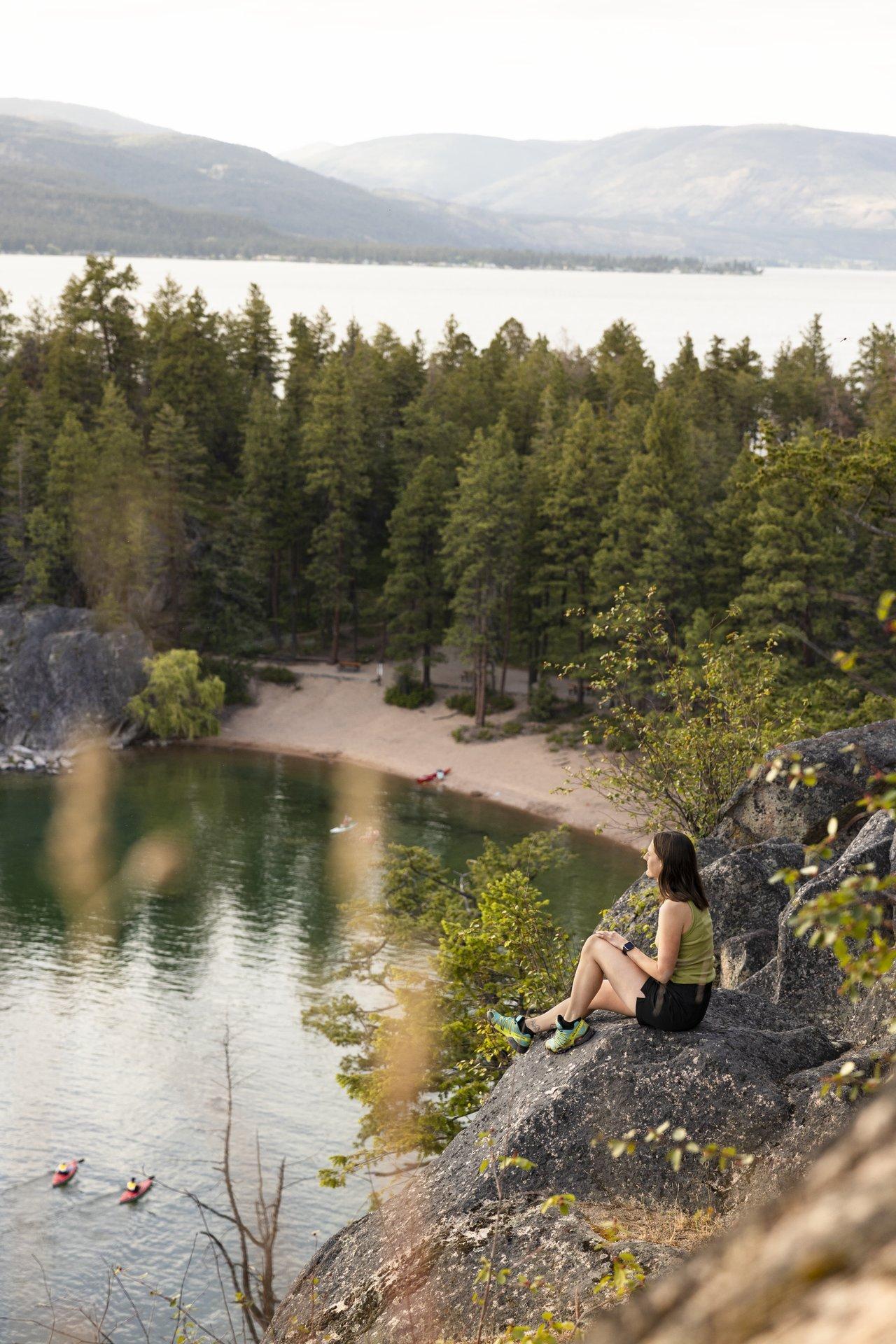 person sitting on rock overlooking a lake and beach at golden hour