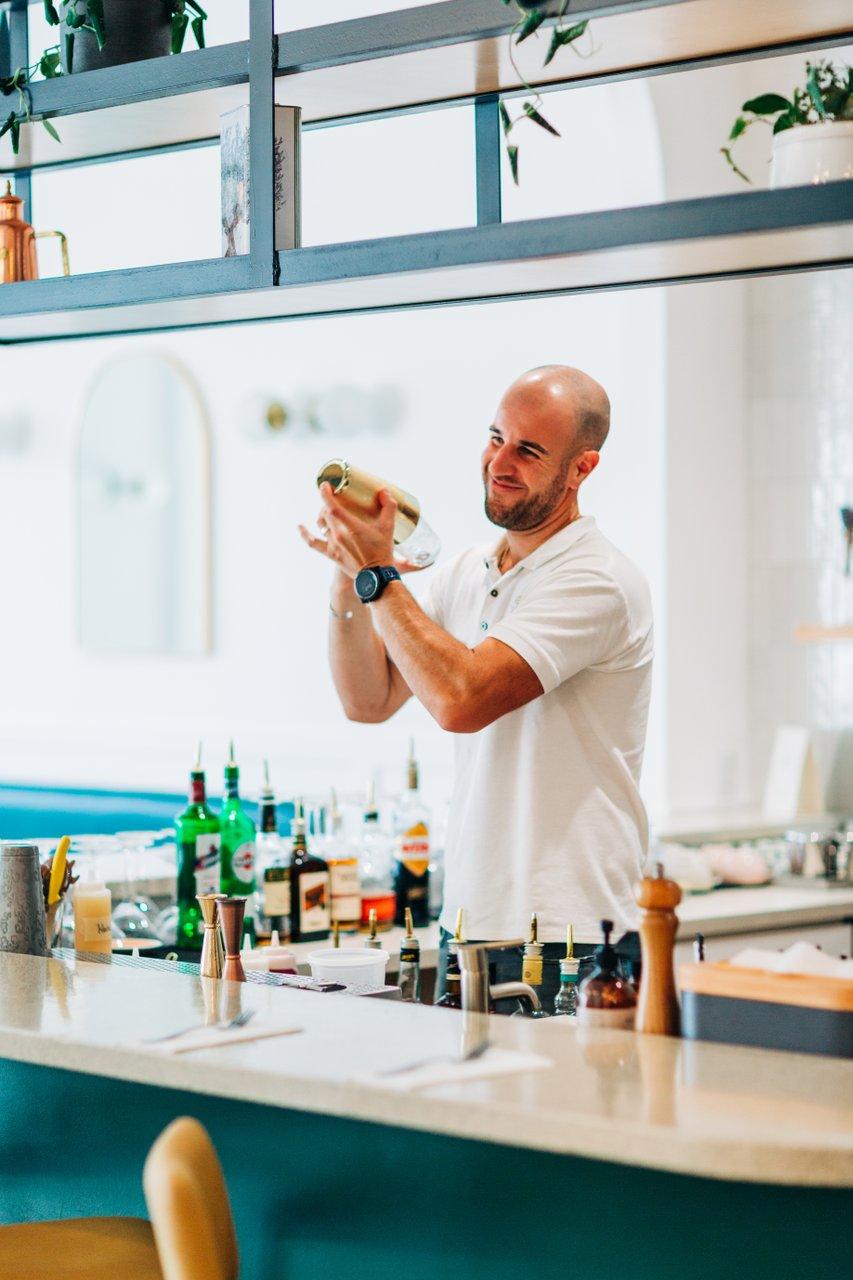 man shaking cocktail shaker behind bar