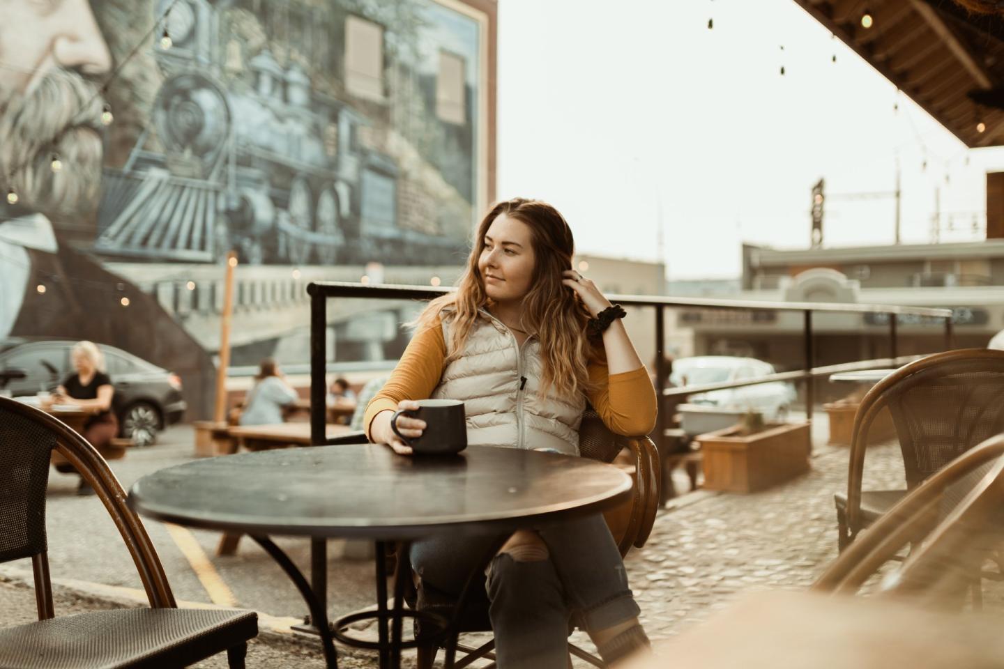 woman sitting outside coffee shop with mural in background