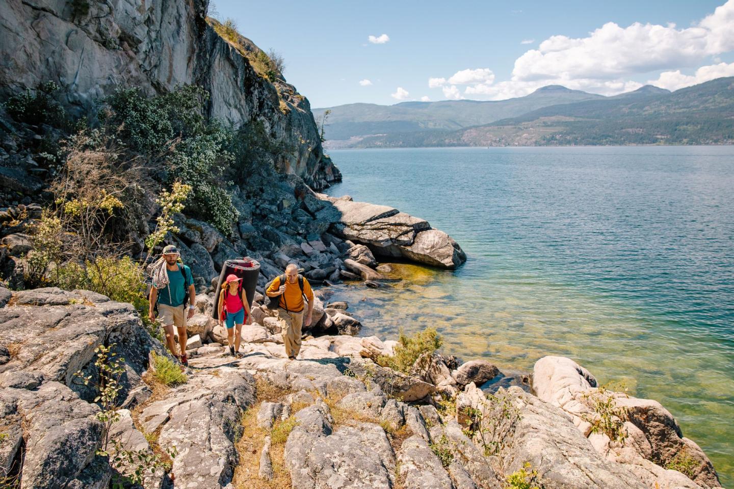 three people walking along a lake with bouldering gear
