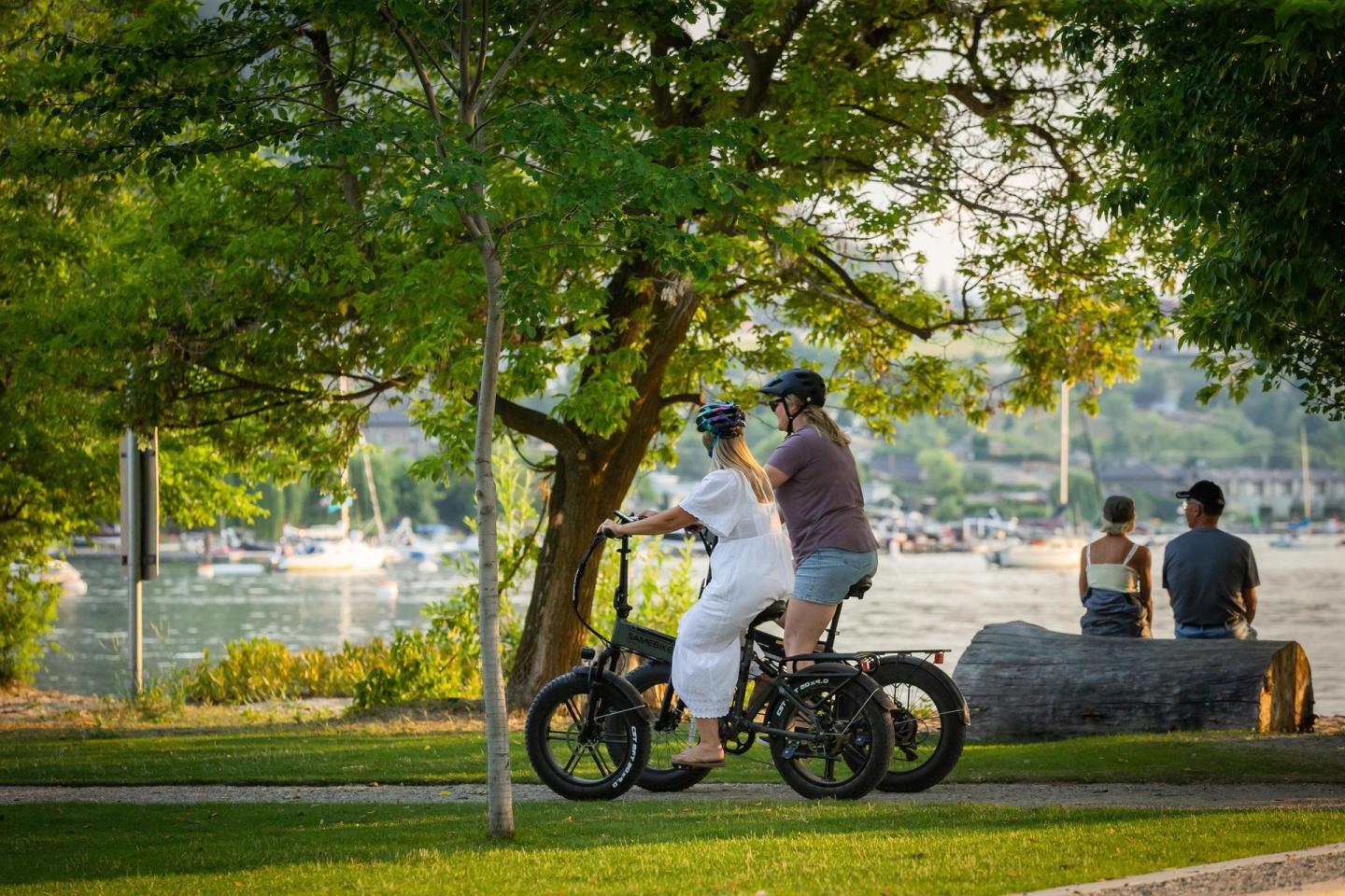 two people riding bikes by lakeside under green trees