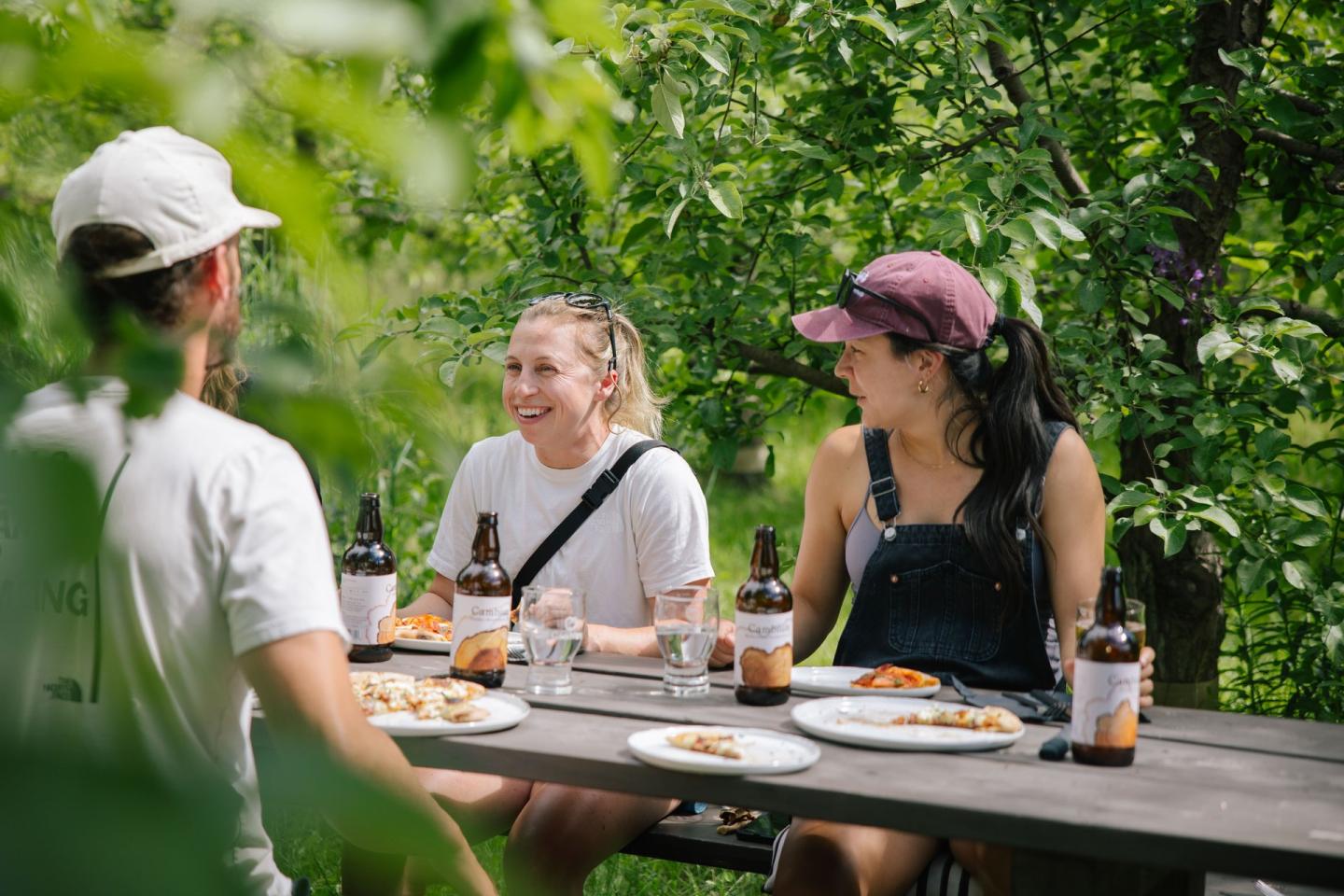 4 people at a picnic table eating pizza in an orchard
