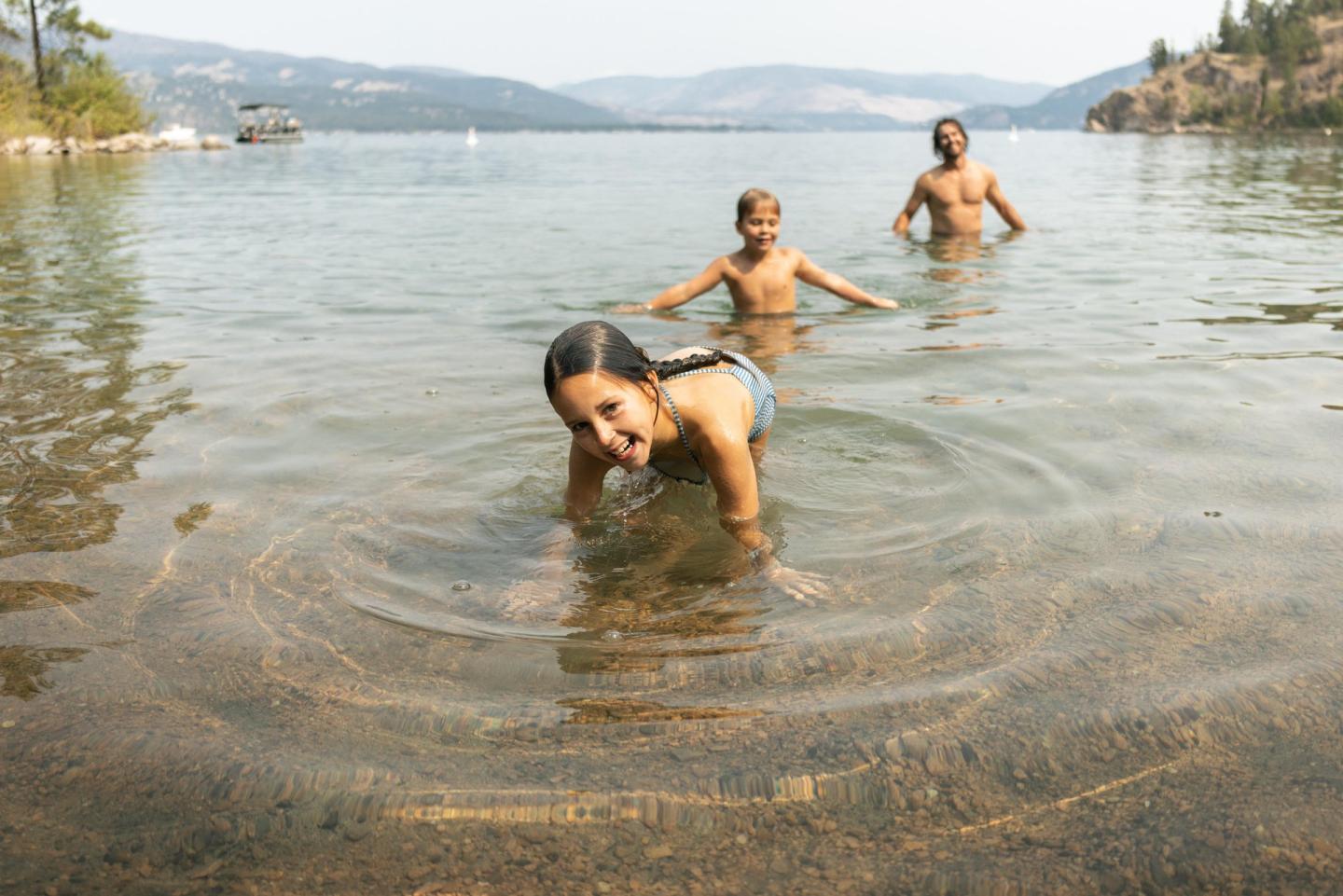 Children playing in a calm, shallow lake with mountains in the background.
