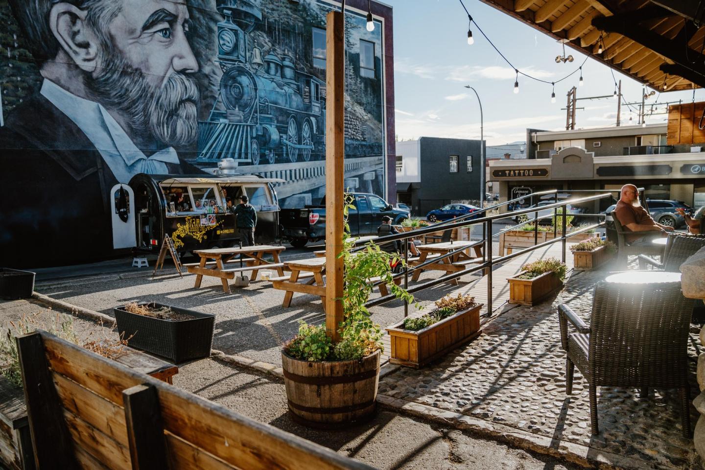 Outdoor seating area with mural, string lights, and sunny atmosphere.