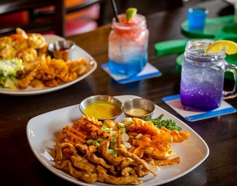 Fried appetizers on a plate with colorful drinks on a table.