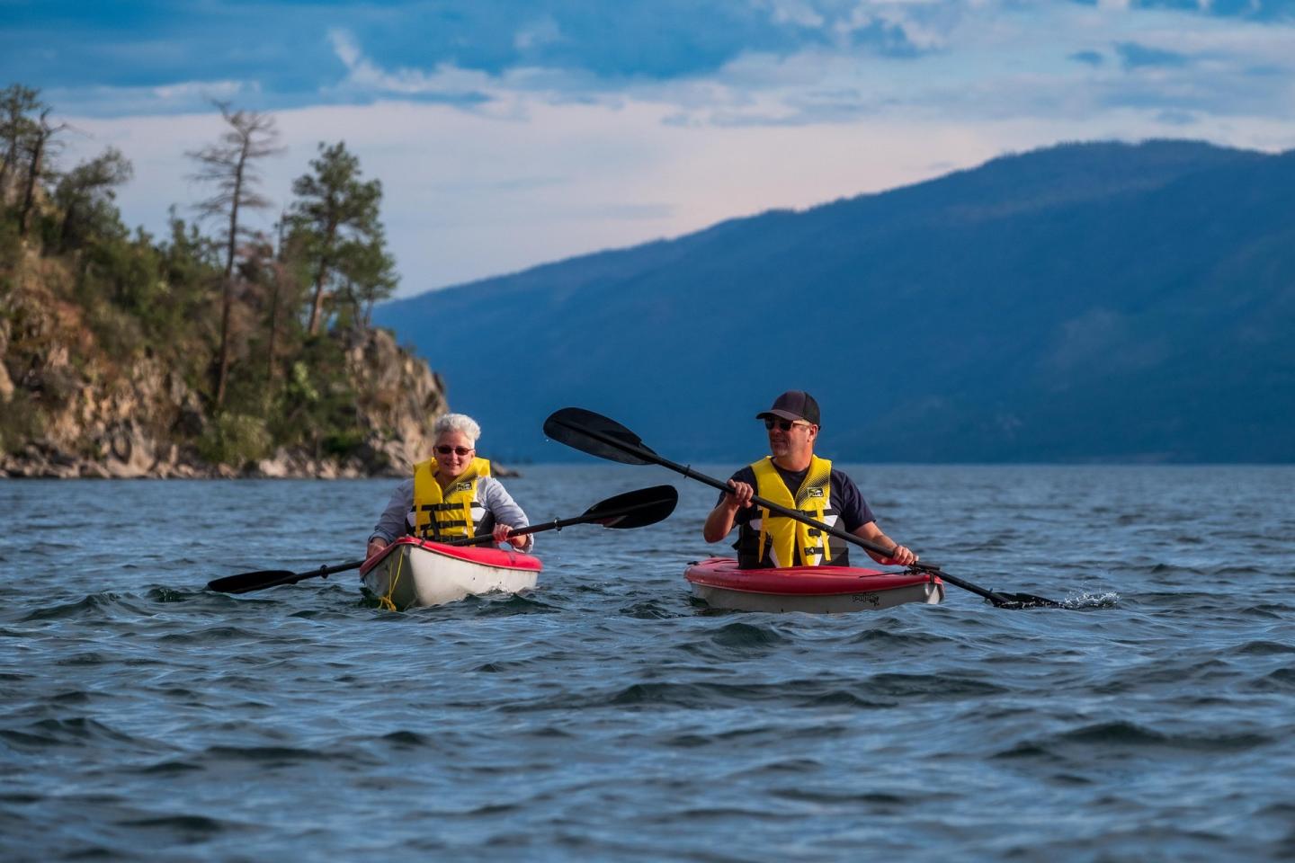 Two people kayaking on a lake with mountains in the background.