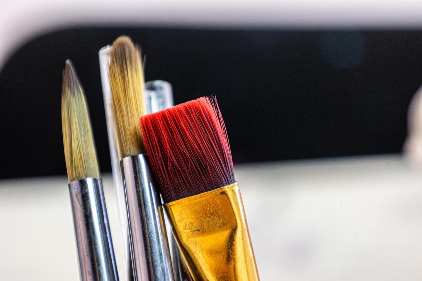 Three paintbrushes, two round and one flat, in close-up.
