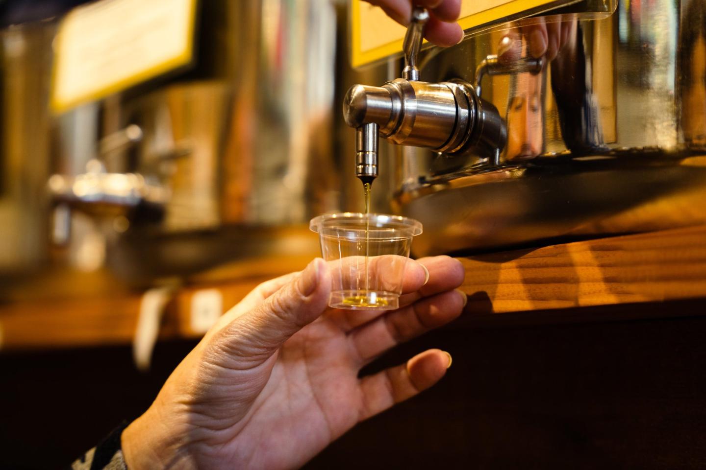 Hand collecting oil sample from a metal dispenser.