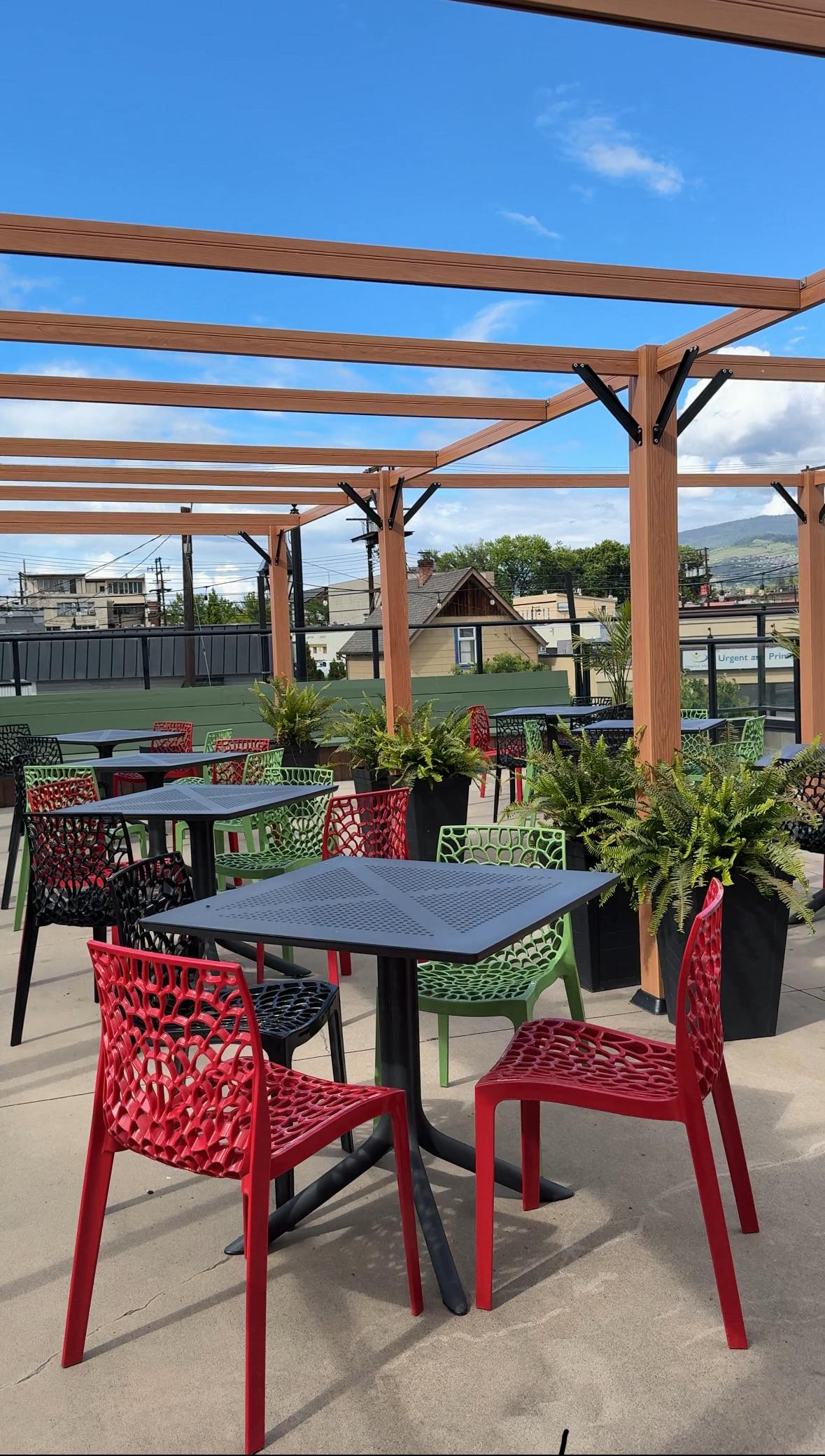 Outdoor patio with red chairs, tables, and pergola under a blue sky.