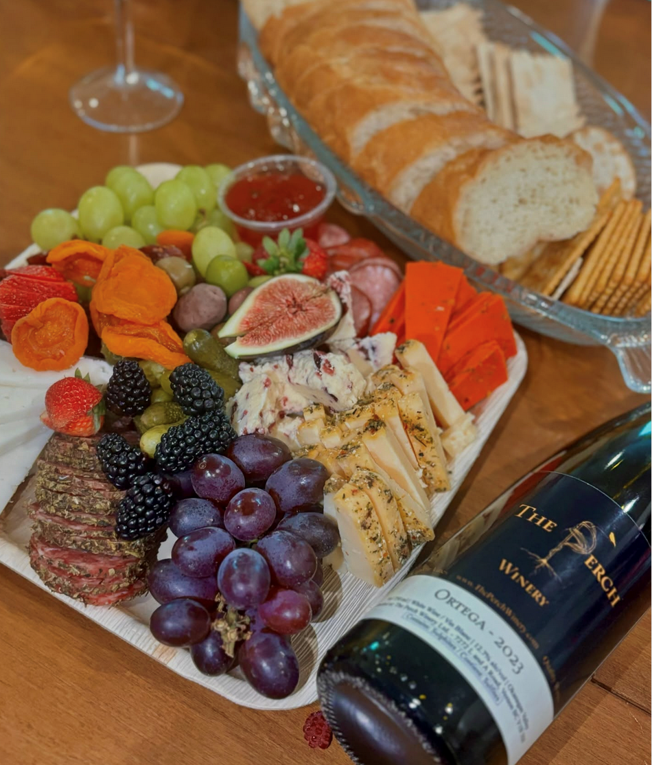 Cheese and fruit platter with bread and red wine on a wooden table.