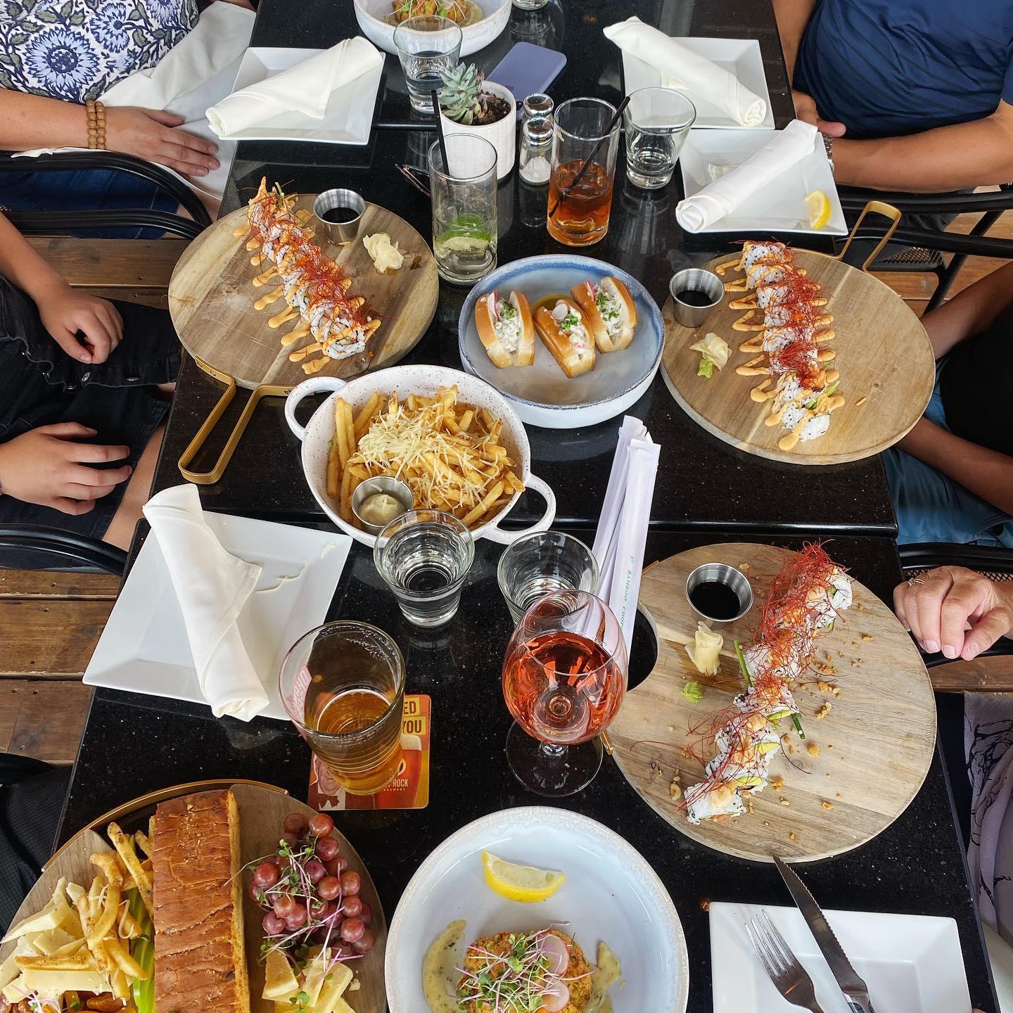 A table with sushi, fries, and drinks on wooden platters.