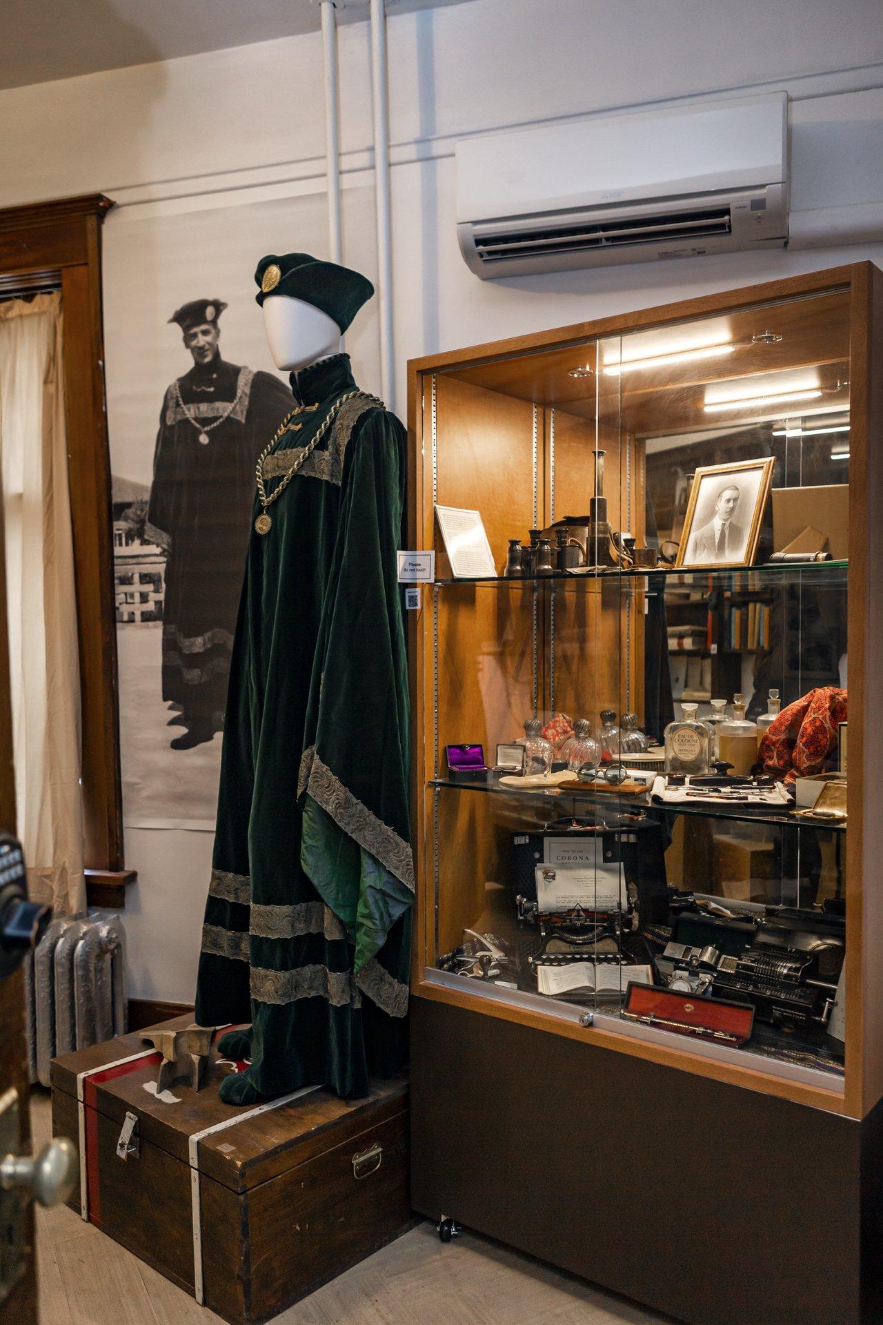Mannequin in green robe beside a glass display case with vintage items.