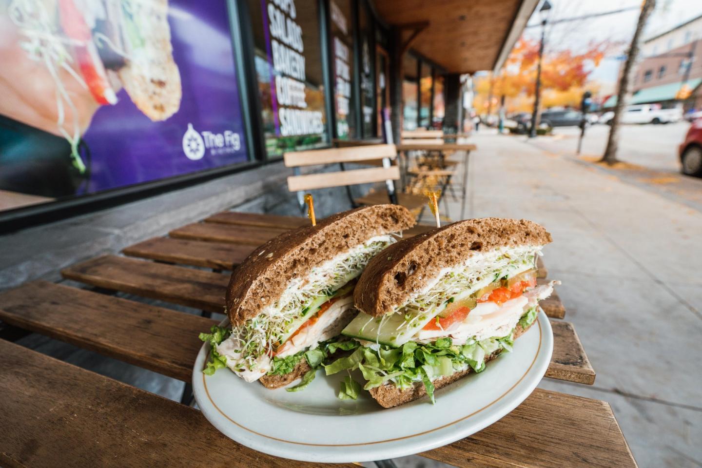 Whole grain sandwich with veggies on a wooden table outside a café.