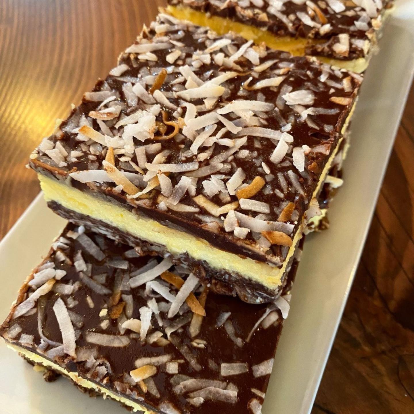 Chocolate coconut bars on a white plate, layered with a yellow filling.