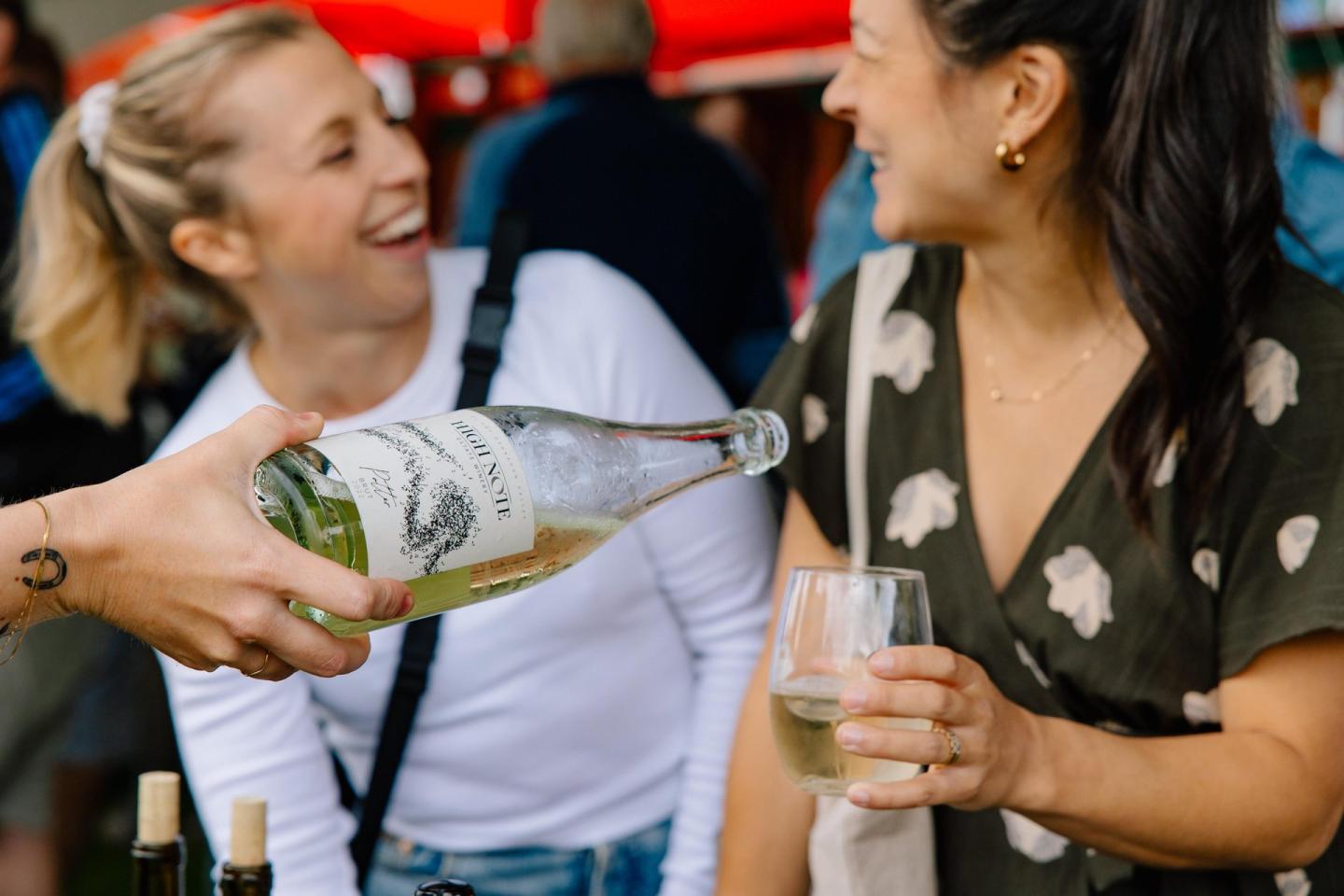 Two women smiling as one pours wine into the other's glass.