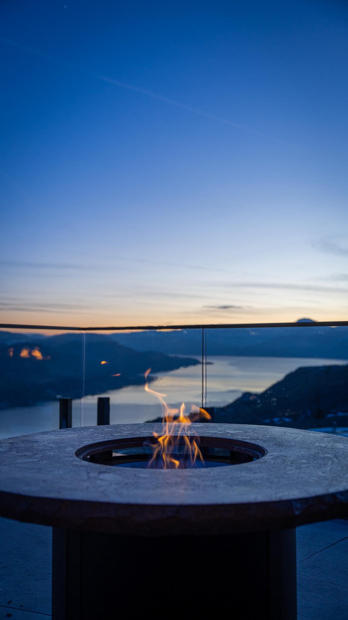 Fire pit on a balcony overlooking a lake at sunset.