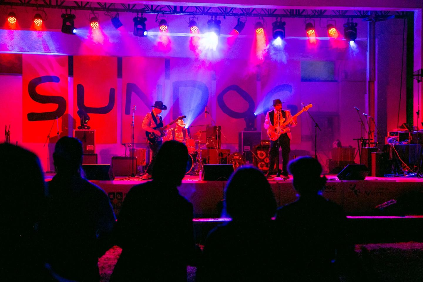 Live band performing on stage with colorful lights and audience watching.