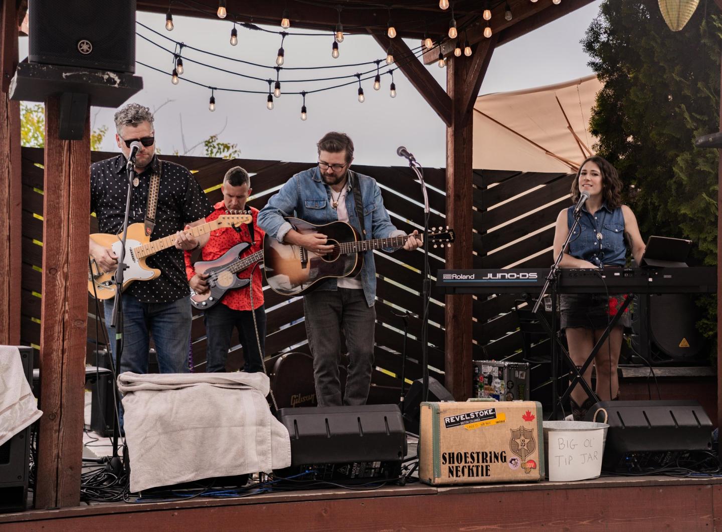 Band playing music on an outdoor stage with string lights above them.