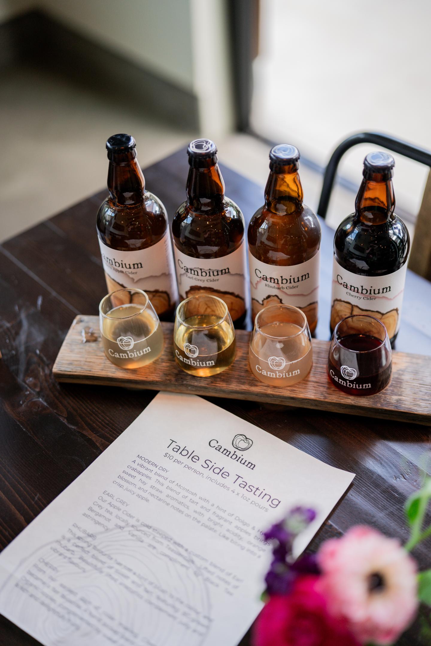 cidertasting flight with four glasses and bottles on a wooden tray, menu underneath.