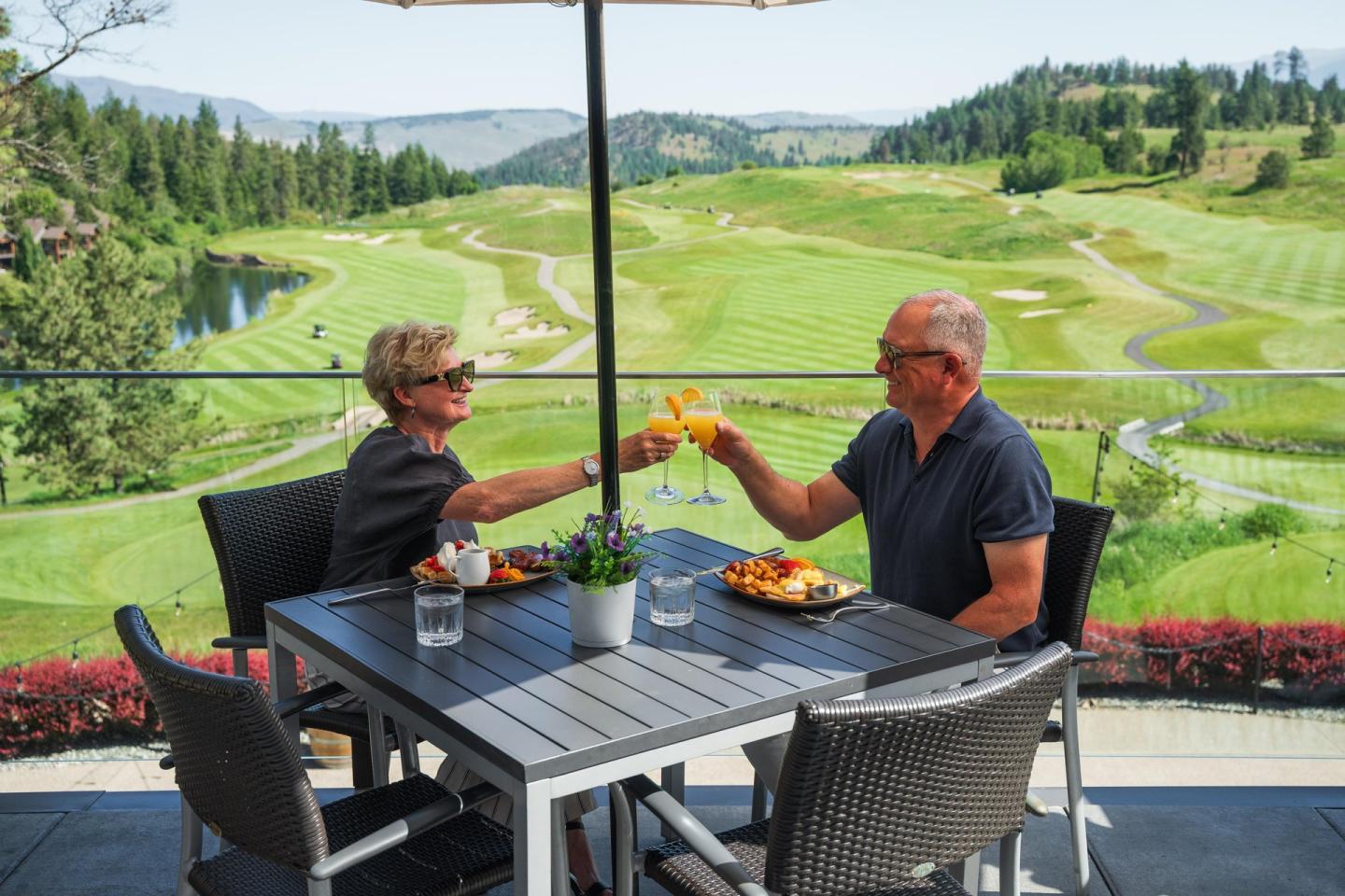 Couple toasting drinks on a patio overlooking a lush golf course.