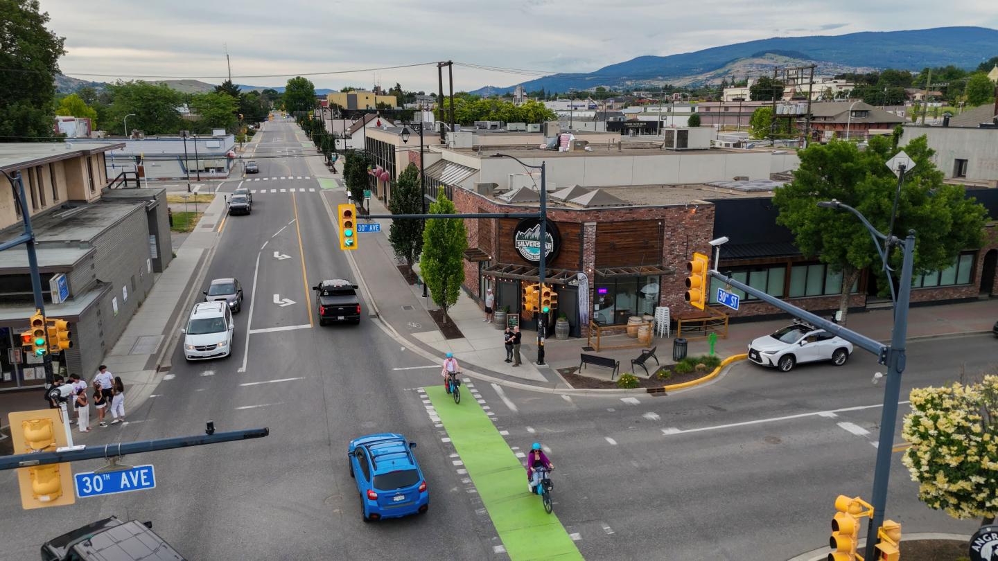 Urban intersection with cars, cyclists, and pedestrians on a cloudy day.