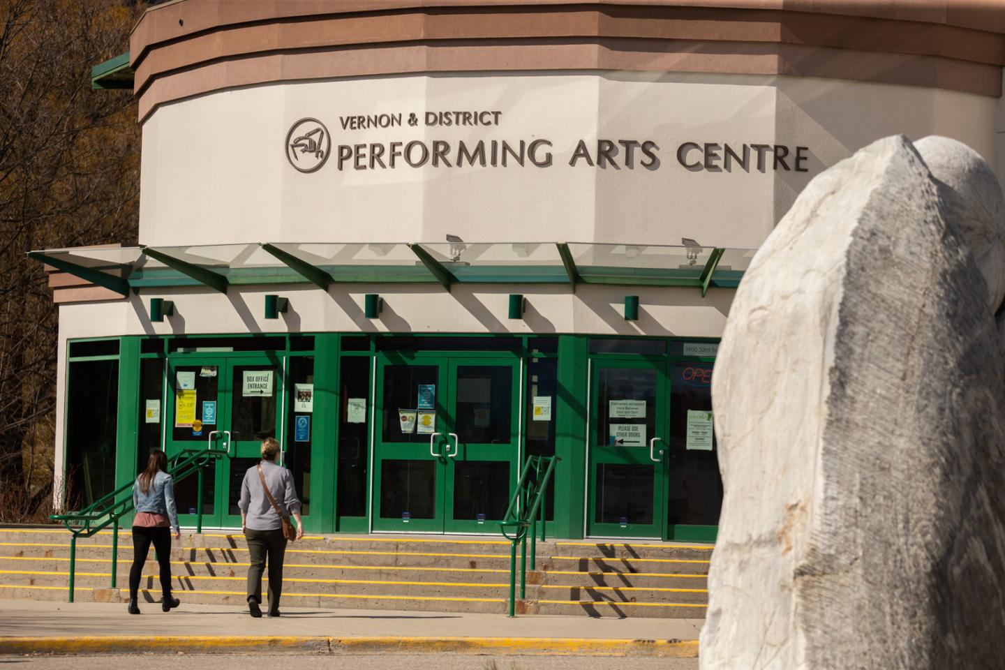 People walking toward a performing arts center with green doors.