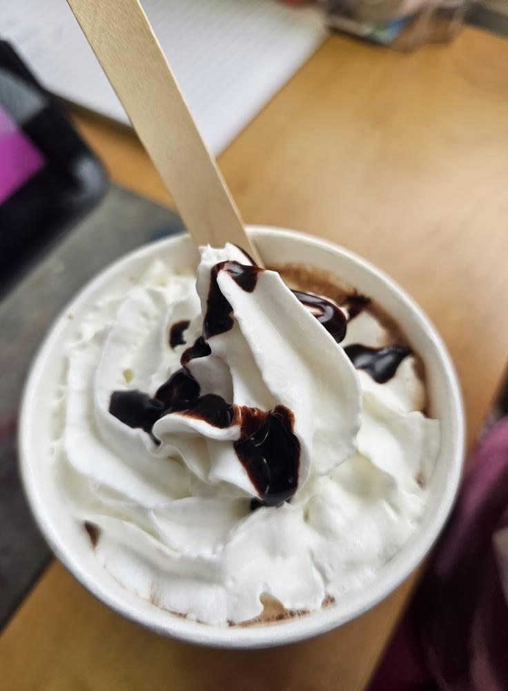 Hot chocolate with whipped cream and chocolate drizzle in a paper cup.