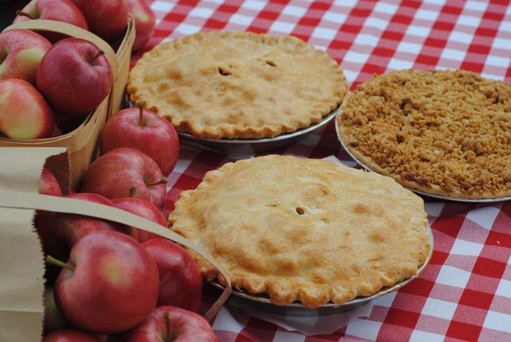 Baked pies and apples on a red and white checkered tablecloth.