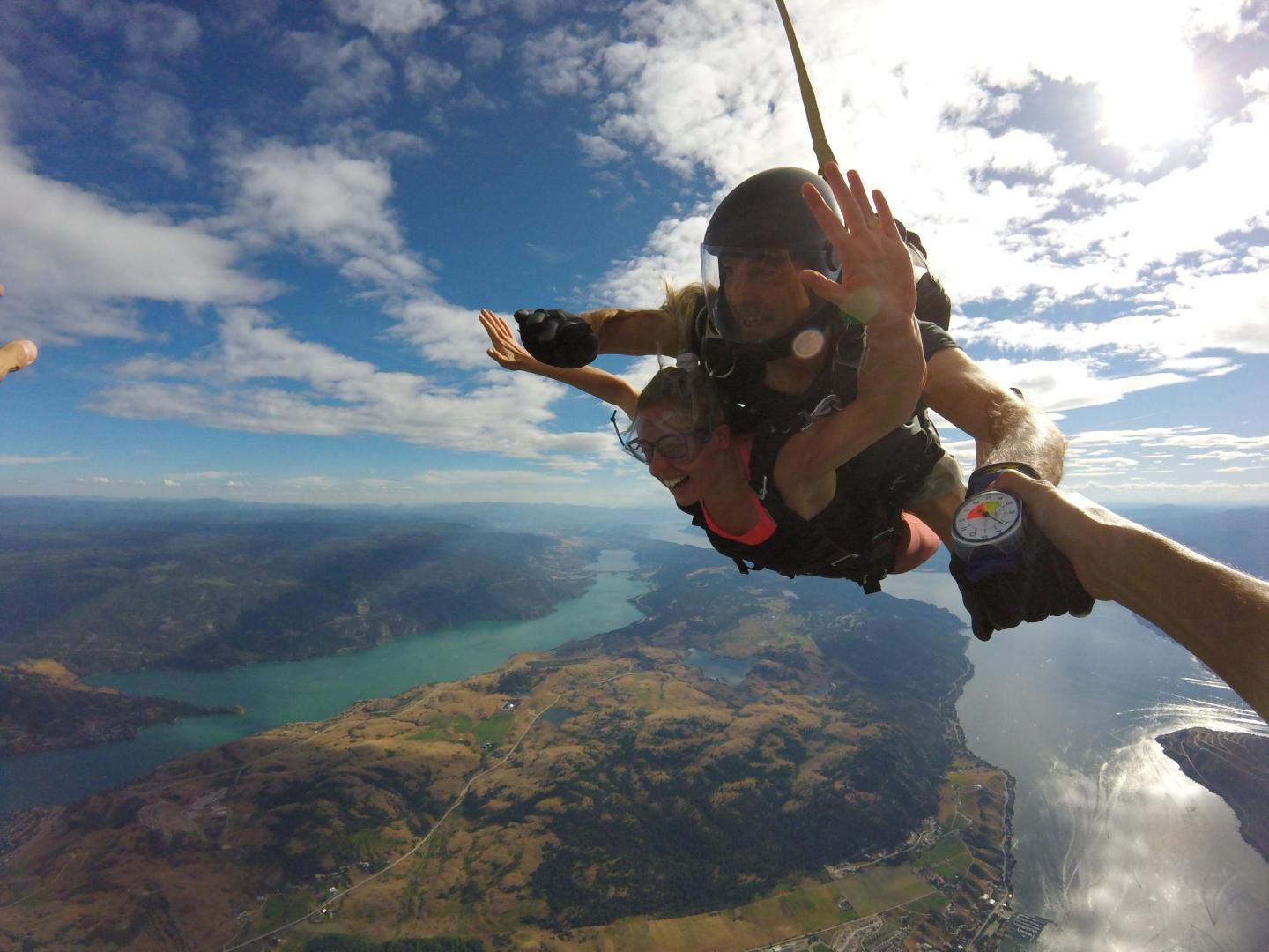 Skydivers tandem jumping over a scenic landscape with lakes and mountains.
