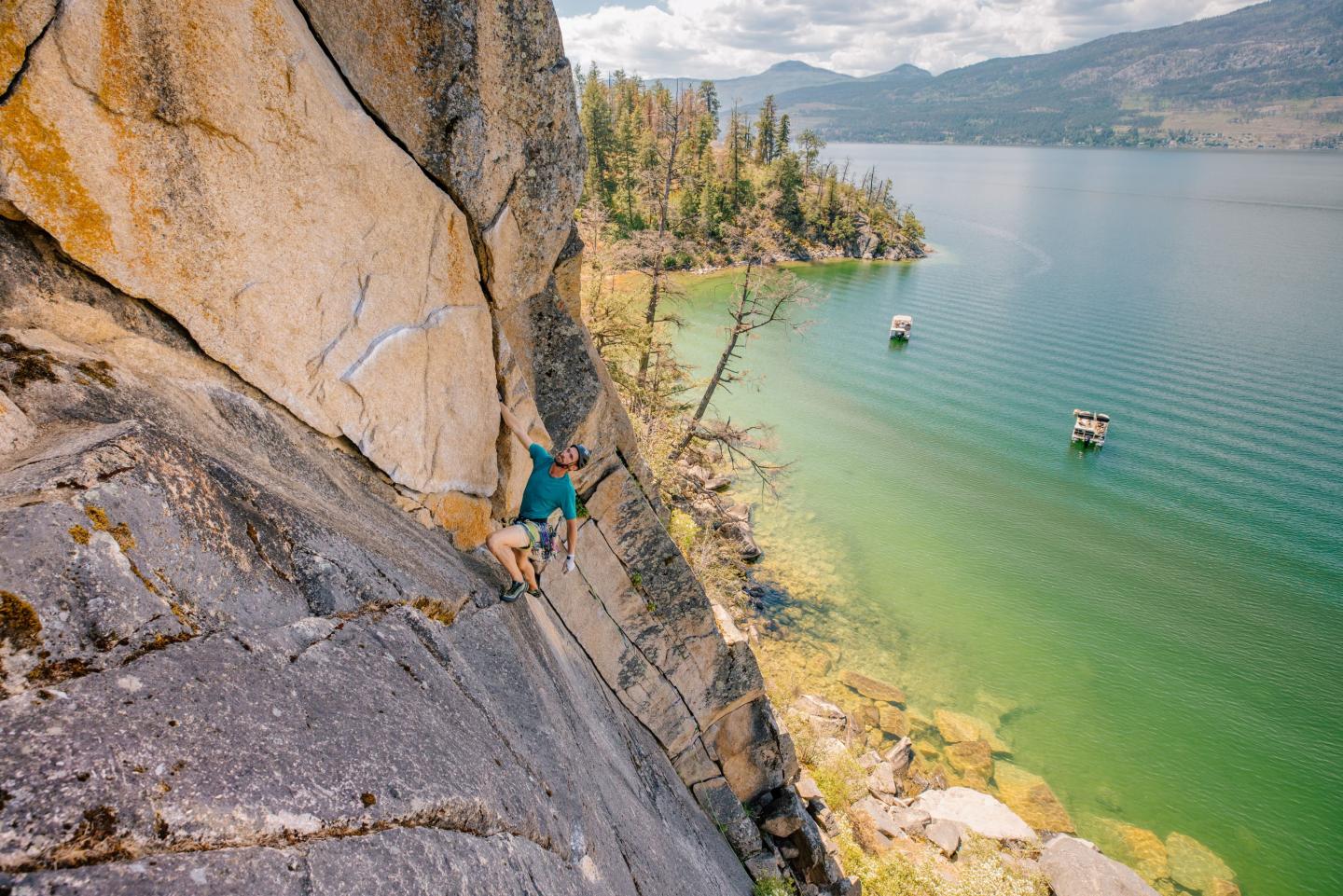 Rock climber scaling cliff above a scenic lake.