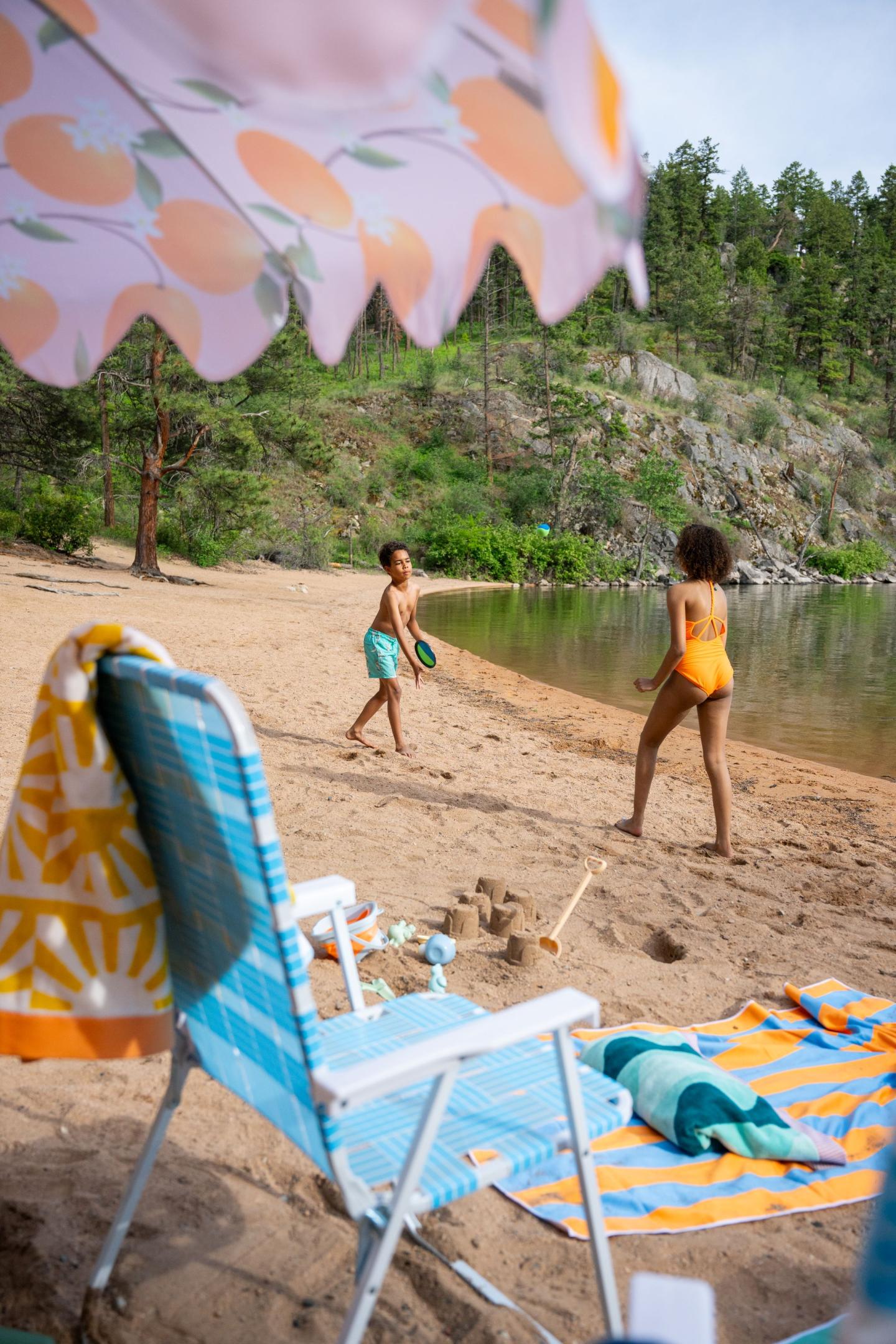 Kids playing on a sandy lakeside beach with chairs and umbrellas.