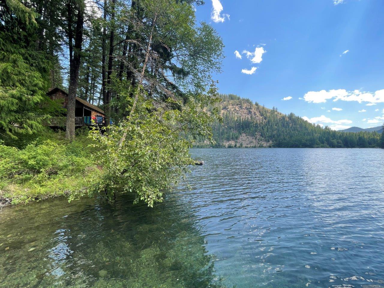 Lake with clear sky, surrounded by trees and distant hills, house on the left.