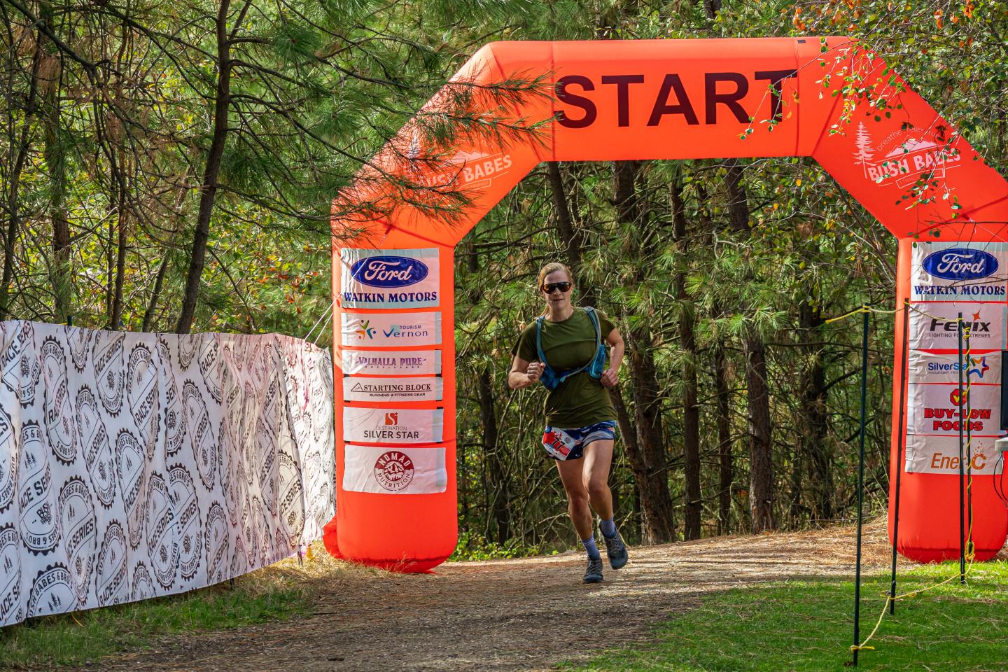 Runner under orange start arch in forest race.