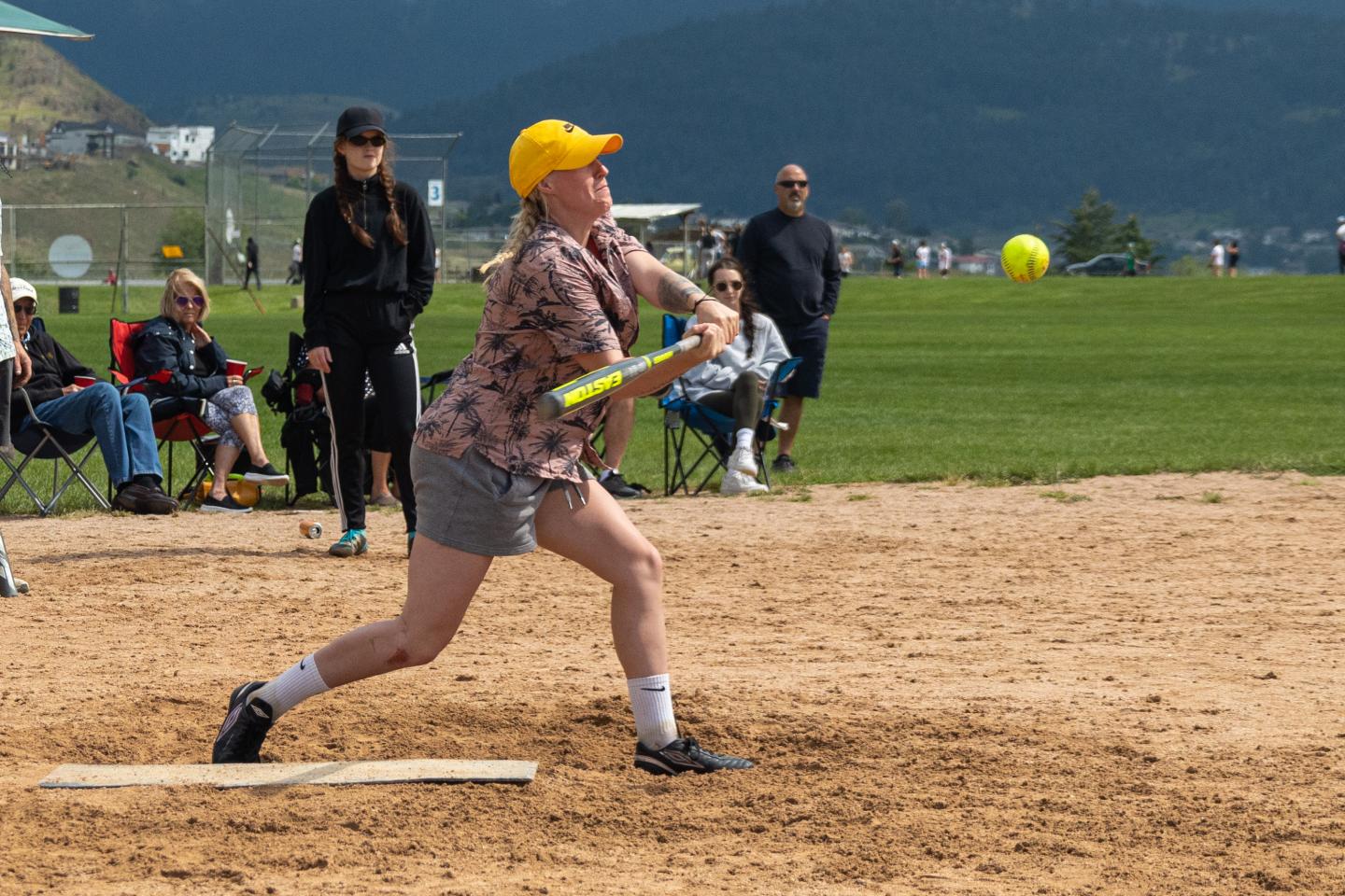Softball player in mid-swing on a sunny day at a park.