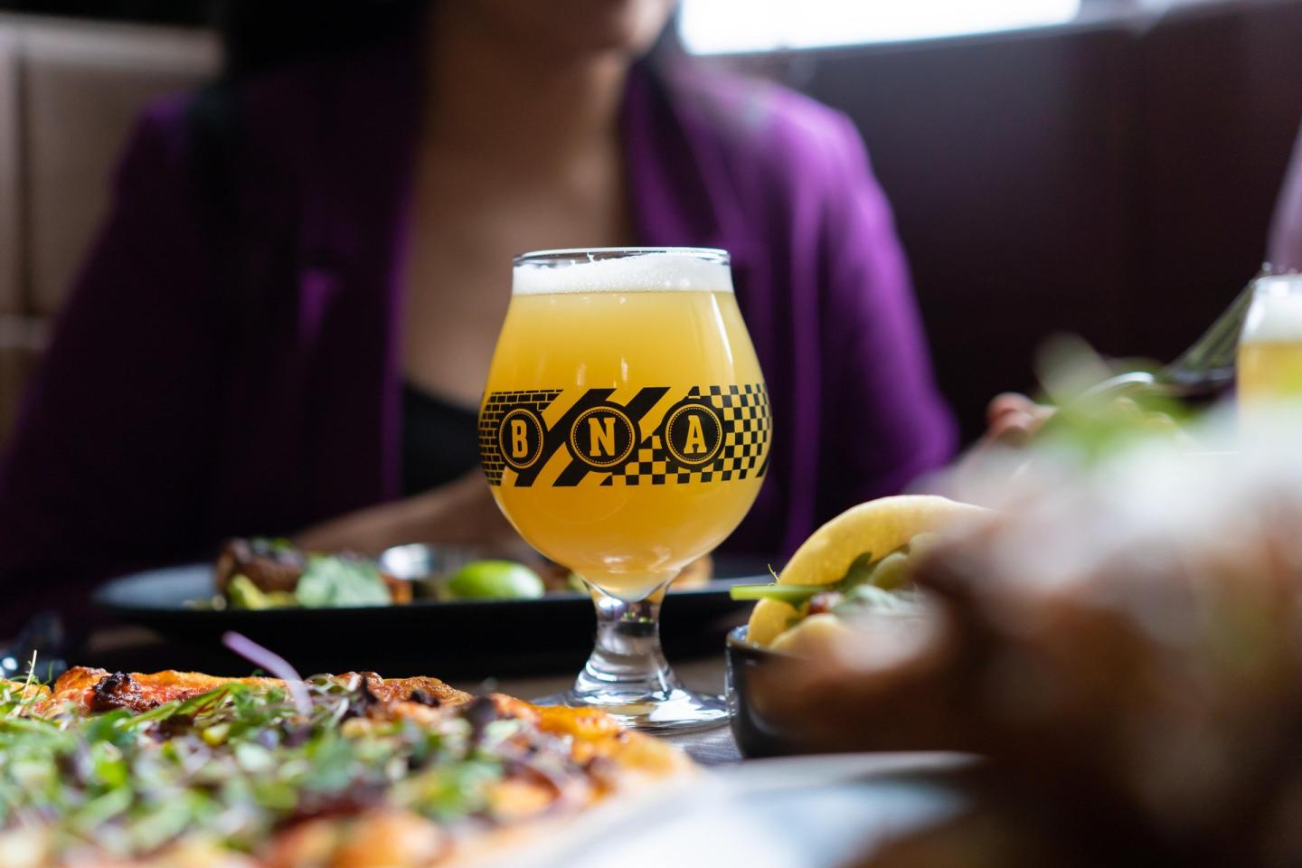 Beer glass on a table with food, person in background.