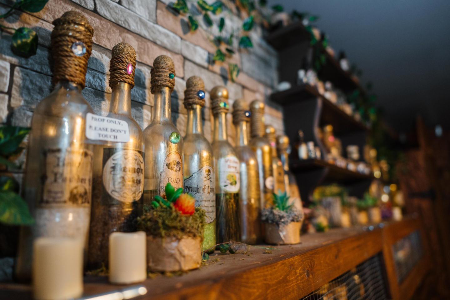 Antique bottles on a wooden shelf, surrounded by candles and greenery.