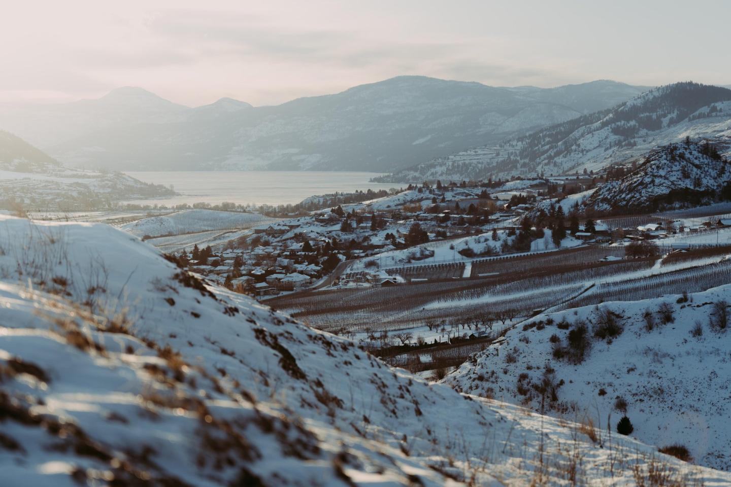 Snow-covered valley with distant mountains under a soft sky.