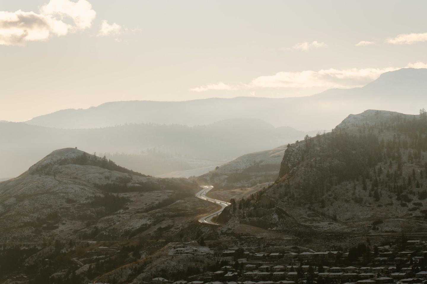 Misty mountains with a winding road under a soft, cloudy sky.