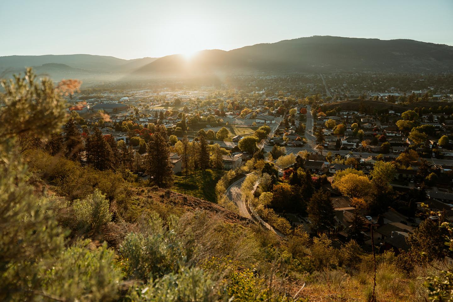 Sunrise over a valley with a town, surrounded by hills and greenery.